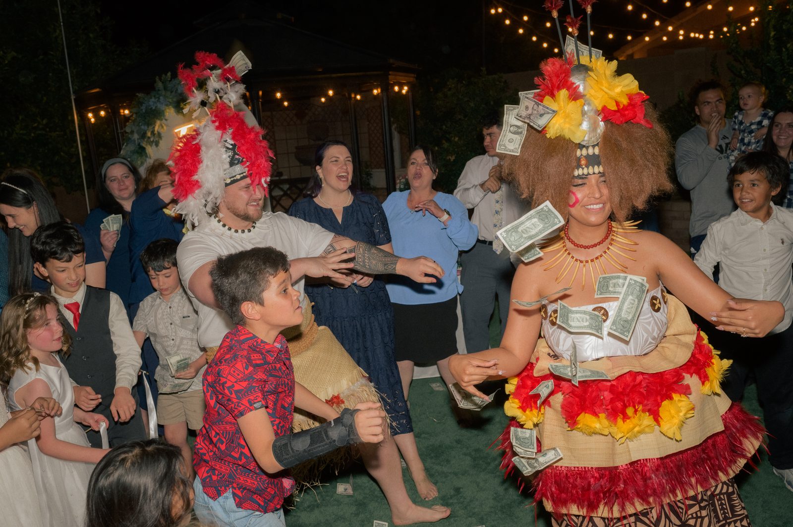 Talia and Enoch dance in Tongan attire at their backyard wedding reception in Arizona as family and guests shower them with bills